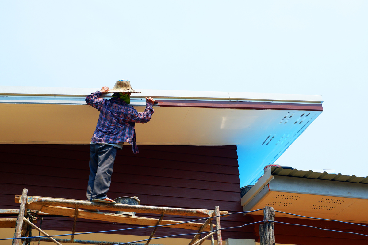 Worker Painting Gutter of House 